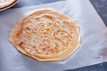 Step-by-step preparation of the festive Russian Kurnik pie, assembling a puff pie with fillings, step 2 - laying out the cooked pancakes on a circle of unleavened dough, selective focus, horizontal © Анна Журавлева