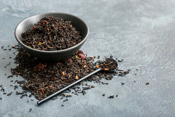 Dry black tea leaves in bowl with spoon on dark background