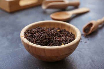 Dry black tea leaves in bowl on dark background