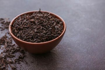 Fototapeta na wymiar Dry black tea leaves in bowl on dark background