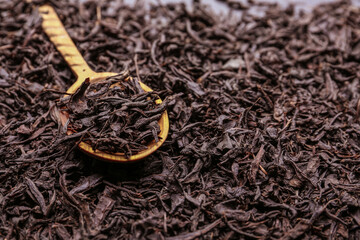 Dry black tea leaves with spoon as background