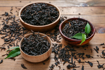 Dry black tea leaves in bowls on wooden background