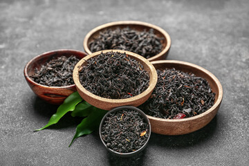 Dry black tea leaves in bowls on dark background