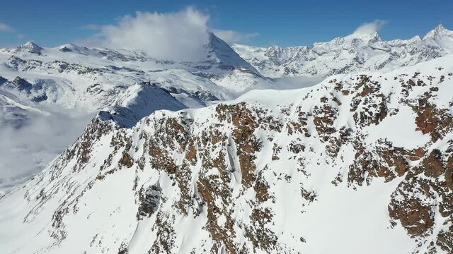 Aerial drone footage of the famous Zermatt ski resort and a steep ridge with the Matterhorn peak half coverd by clouds in Canton Valais in Switzerland