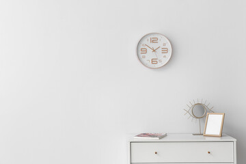 Blank photo frame, mirror and magazine on table against light wall with clock in room
