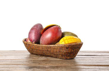 Basket with sweet ripe mangoes on table against white background