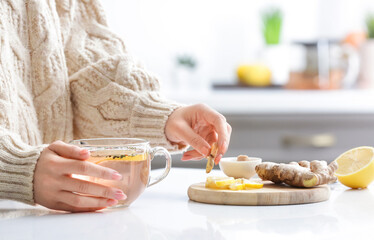 Woman making healthy tea with ginger and lemon in kitchen