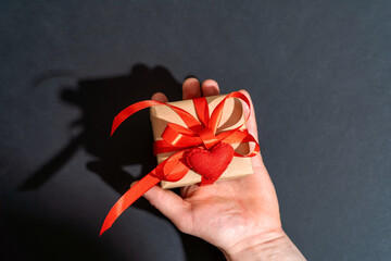 Top view, a man holding a gift box wrapped in kraft paper with a red ribbon and a felt heart