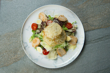 Top view of Traditional Italian Caesar salad served on marble plate. Salad with bread croutons, grilled chicken fillet slices, fresh lettuce, quail eggs, cherry tomatoes on stone background. Flat lay
