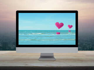 Pink fabric heart love air balloon on tropical sea with desktop modern computer monitor screen on wooden table over modern city tower and skyscraper at sunset sky, vintage style, Business internet dat