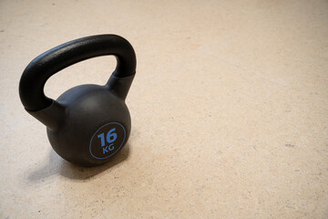 Naklejka na ściany i meble Black metal kettlebell 16 kg covered with rubber on the floor. Home workout background.