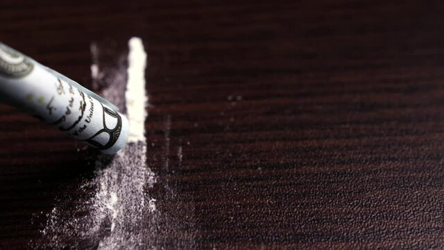 POV close-up shot of a line of cocaine powder sniffed up by a rolled-up dollar bill on a dark countertop. Concept of addiction and substance abuse