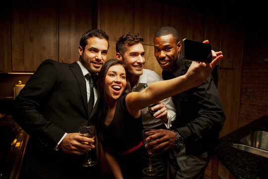 Friends drinking in kitchen at party and taking photographs