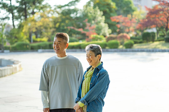 秋の公園にたたずむ笑顔の日本人シニア夫婦
