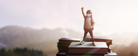 concept: girl on giant books on top of mountain dreaming of going back to school with mask during...