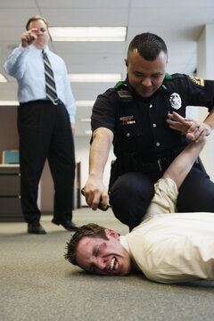 Police officer holding beat up businessman on floor in office