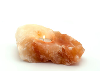 Burning tea-light candle in a salt stone holder on white background