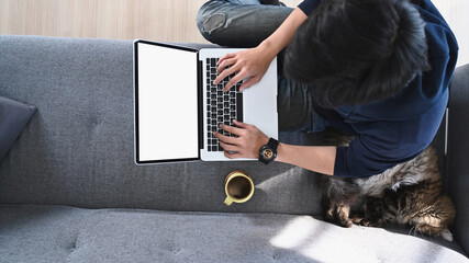 High angle view of man using laptop computer while sitting with his cat on comfortable couch.