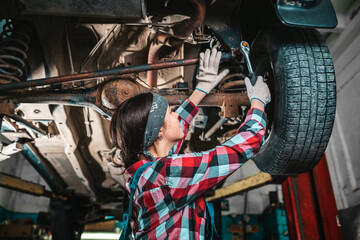 Portrait of a young female mechanic in uniform and gloves who repairs a car. The car is on the...