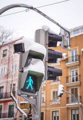 Traffic light with snow on a street in Madrid. The green crosswalk signal is on. Snowing during “Filomena” storm. 