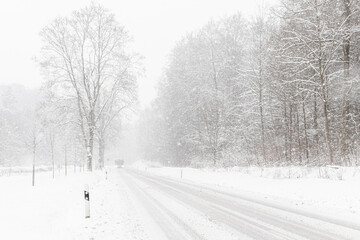 Heavy snowfall on the road. Winter landscape with a rural street leading into the forest. Weather, transport, season concept