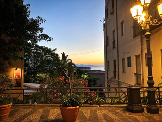 Late summer evening. Street lights, flowers, pots. Beautiful view of the sea and the mountains in...