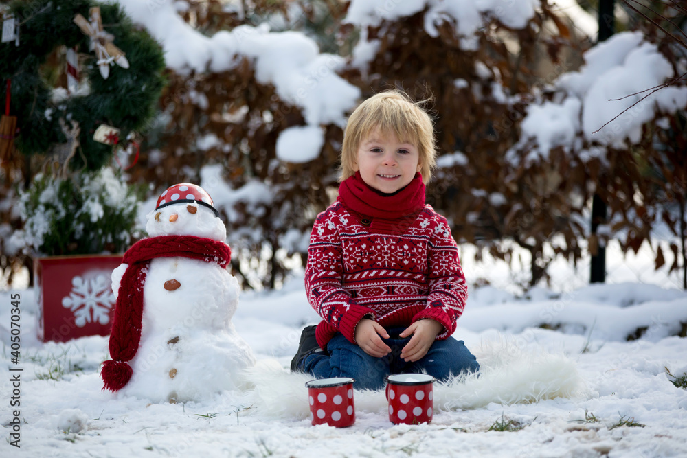 Sticker Sweet blond toddler child, boy, playing in garden with snow, making snowman, happy kid winter time