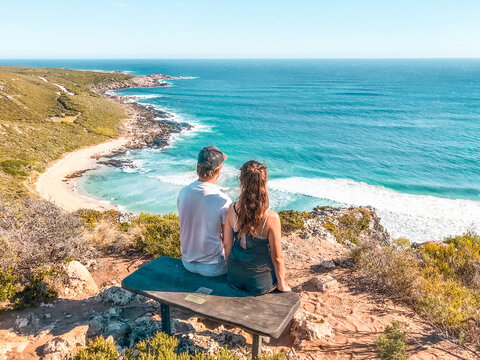 Man and woman sitting on bench on mountain island facing the ocean
