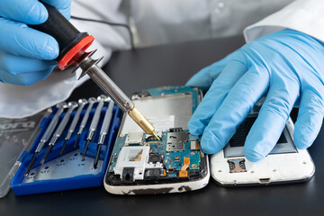Technician repairing inside of mobile phone by soldering iron. Integrated Circuit. the concept of...
