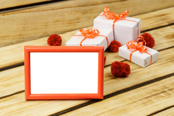 Blank mock up photo frame on wood background. White gifts are tied with a red ribbon.