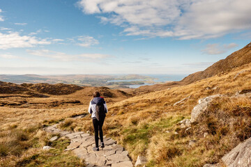Teenager girl on a path on a mountain walk, Diamond hill in Connemara National park, county Galway, Ireland, Bright sunny day, blue cloudy sky. Hiking and outdoor activity. Popular tourist spot.
