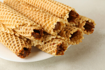 Plate with wafer rolls with condensed milk on white textured background