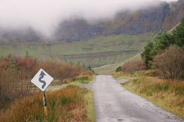 Small narrow road into mountains by a green forest. Gleniff horseshoe drive loop, County Sligo, Ireland. Low cloudy sky. Travel concept