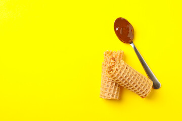 Wafer rolls and spoon with condensed milk on yellow background