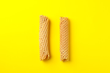 Tasty wafer rolls with condensed milk on yellow background