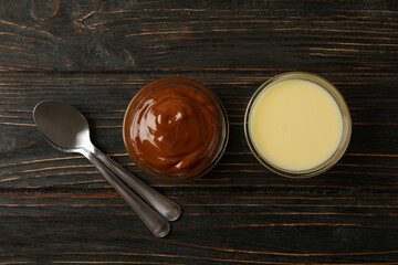 Spoons and bowls with condensed milk on wooden background