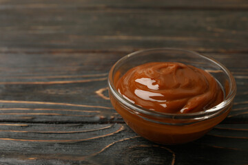 Glass bowl with caramel condensed milk on wooden background
