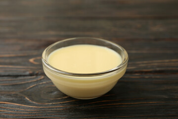 Glass bowl with condensed milk on wooden background