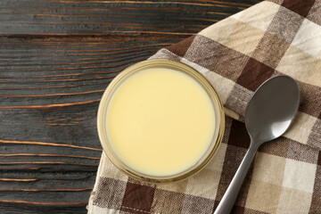 Towel, spoon and bowl with condensed milk on wooden background