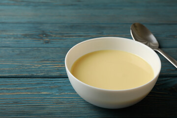 Spoon and bowl with condensed milk on wooden background