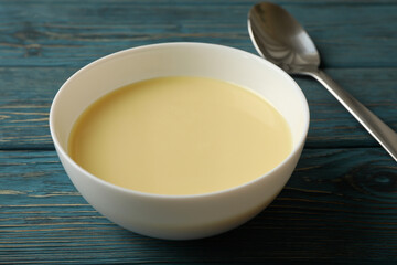 Spoon and bowl with condensed milk on wooden background
