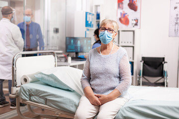Senior woman waiting for doctor consultation in hospital wearing face mask in the course of covid19. Global health crisis, medical system during pandemic with coronavirus, sick elderly patient in