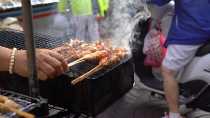 Grilled chicken with wooden stick on charcoal grill at street market in Bangkok, Thailand