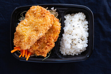 Japanese deep fried pork with rice or tonkatsu set in a lunch box on black background.