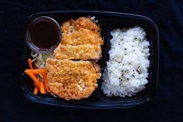 Japanese deep fried pork with rice or tonkatsu set in a lunch box on black background.