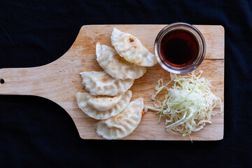 Japanese grilled gyoza dumplings with soy sauce on a wooden plate.