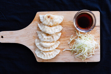 Japanese grilled gyoza dumplings with soy sauce on a wooden plate.