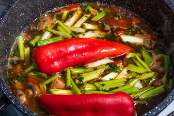 Cooking spicy pork stew with mushrooms in oriental style in a saucepan with spices, hot peppers and green onions - top view, close-up