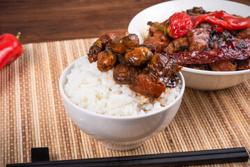 Spicy stewed pork with mushrooms in oriental style with spices, hot pepper with boiled rice in a bowl and and a cup with meat on a bamboo napkin and chopsticks - top view, close-up