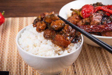 Spicy stewed pork with mushrooms in oriental style with spices, hot pepper with boiled rice in a bowl and and a cup with meat on a bamboo napkin and chopsticks - top view, close-up